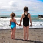 Two girls standing on the beach looking at the waves